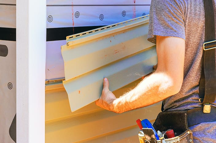 Construction worker installs siding on house during sunny afternoon in residential area